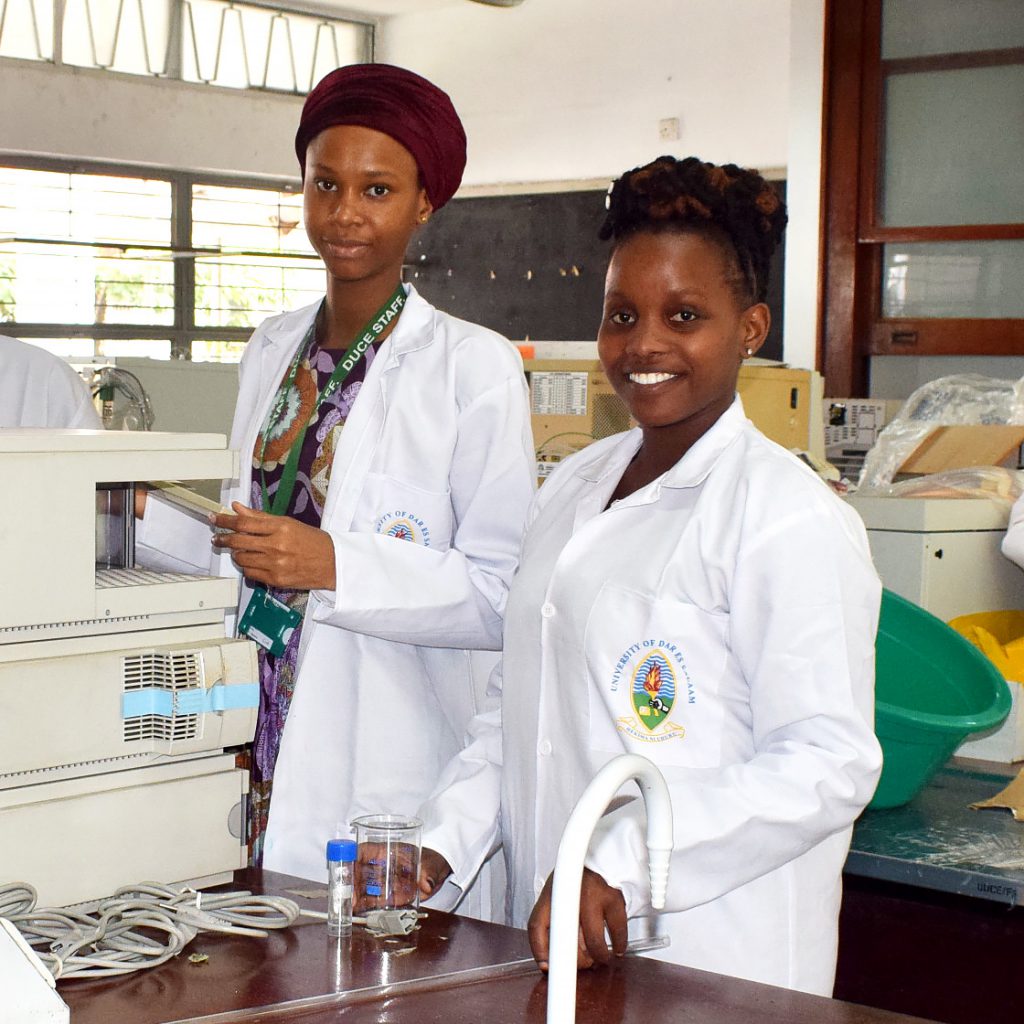 A couple of female researchers from Dar Es Salaam university smiling to the camera in front of equipment